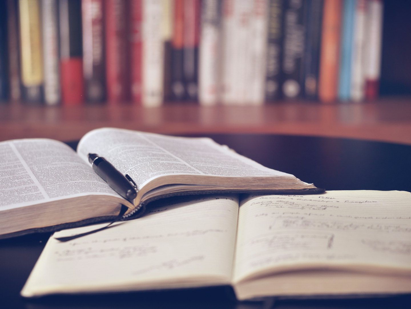 Un libro aperto e un taccuino con una penna su una scrivania di legno scuro.